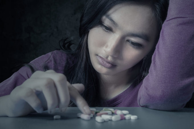 Portrait of teenge girl choosing pills with stressful expression, symbolizing a drugs addict