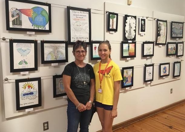 OH Clim-ACT-ivists Club president Anya Al-Salem (right) poses with OH art teacher Ms. Chrisanthy Vargo at the climate change themed art exhibit displaying OH students artwork at Daggerwing Nature Center last year.