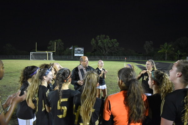 Soaking wet from the traditional championship dousing, Olympic Heights girls soccer head coach Jim Cappello addresses his team while holding the District 13-6A championship trophy.